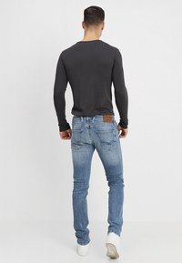Men's fitted long-sleeve gray shirt paired with light blue faded denim jeans, featuring back pockets and a brown leather patch at the waistband.