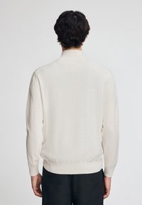 Ljus krämfärgad tröja gjord av mjukt stickat material, med rund halsringning och ribbade ärmslut och fåll. Enkelt och minimalistiskt design.