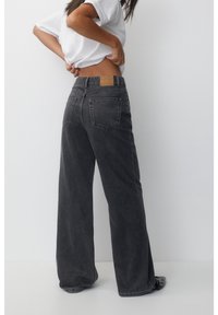 Tummanharmaat leveälahkeiset farkut korkealla vyötäröllä, joissa on nahkainen merkki takavyötäröllä ja kaksi takataskua.