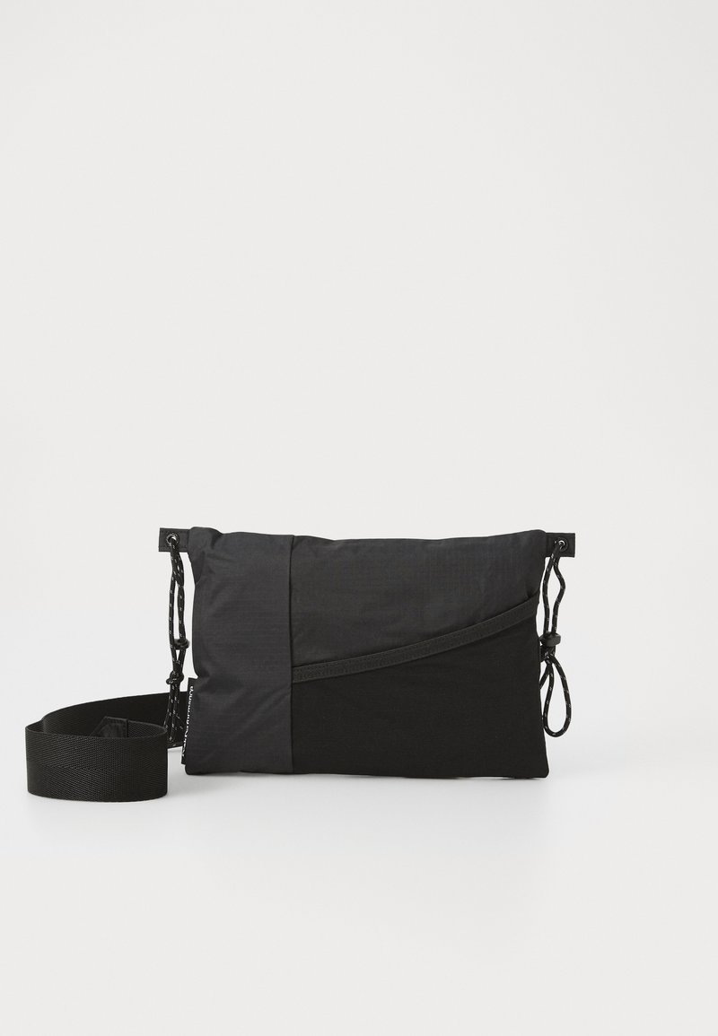 Sac à main noir en tissu texturé, présentant un design diagonal, une bandoulière réglable et des fermetures à cordon sur les côtés.