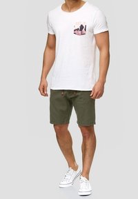 Witte crew neck t-shirt met palmboom graphic op de zak, gecombineerd met olijfgroene shorts en witte sneakers. Eenvoudige casual outfit.