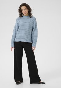 Light blue knitted sweater with a round neck and openwork pattern, paired with wide-leg black trousers and black flat shoes.