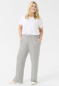 White t-shirt paired with high-waisted, wide-legged pants featuring black and white stripes, side pockets, and a drawstring waistband.