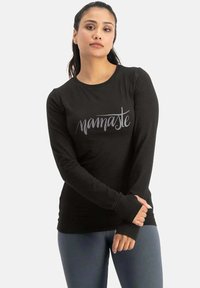 Schwarzes Langarmshirt mit "Namaste" in Grau bedruckt. Hat einen runden Halsausschnitt und eine figurbetonte Passform. Weicher, dehnbarem Stoff.