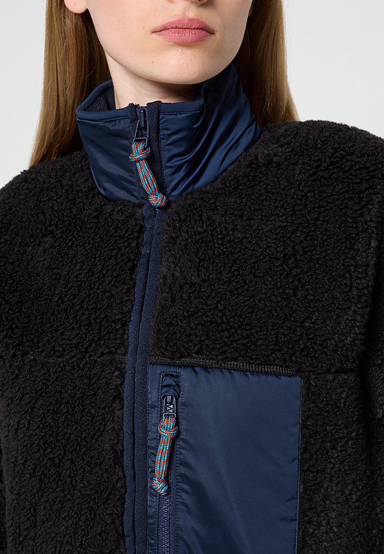 Fleecejacke mit hohem Kragen, schwarzem Strickstoff, marineblauem Einsatz und Reißverschluss. Mit einem hellen Akzent am Reißverschluss und geripptem Saum.