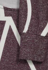 Tessuto testurizzato color marrone scuro con un motivo geometrico bianco, che presenta un design a contrasto per il colletto e i polsini. Texture morbida e lavorata a maglia, vista ravvicinata.