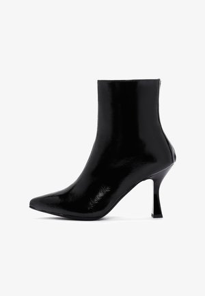 Botín de piel sintética negra con punta afilada, tacón alto y delgado, y superficie lisa y brillante; caña alta con cierre de cremallera en la parte trasera.