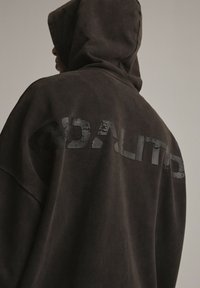 Przesadna bluza z kapturem w ciemnoszarym kolorze. Posiada gładką fakturę oraz postarzony logo umieszczony na plecach.