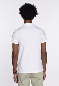 Camisa polo blanca con cuello, mangas cortas y un corte relajado. Presenta un detalle mínimo con una textura lisa.