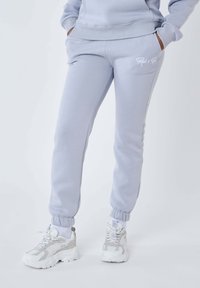 Lichtgrijze joggingsbroeken van zacht materiaal, met een elastische tailleband en boorden, zijzakken en een subtiele witte logodetail.