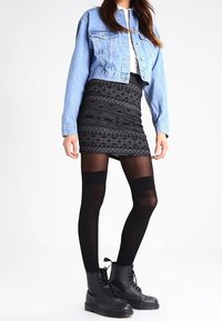 Džínová krátká bunda, bílý top, černá mini sukně s potiskem, černé punčochy nad stehna a černé krajkové vojenské boty.