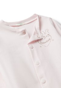 Prenda de bebé de algodón rosa con cierre de botones, que presenta un gráfico de un conejito y el texto "benetton" en un corazón. Tela suave y textura lisa.