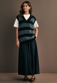 Mørkeblå og grå stribet strikvest med V-hals, lagd over en hvid t-shirt og parret med en sort nederdel og sorte flade sko.