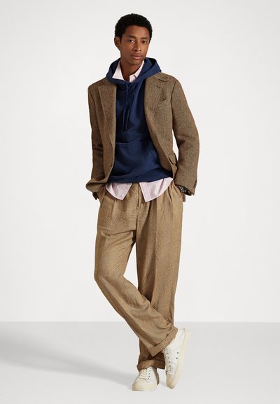 Svetlo rjav blazer z houndstooth vzorcem, oblečen čez mornarsko modro kapuco in svetlo roza srajco, v kombinaciji z bež hlačami z vzorcem in belimi supergami. Teksturni material.