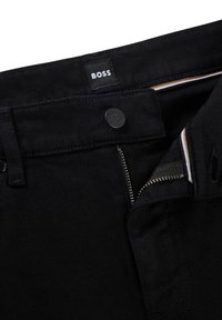 Black denim pants with a button and zip fly closure, featuring a label with "BOSS." Includes accent stitching and a smooth texture.