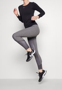 Maglietta sportiva nera a maniche lunghe con scollatura rotonda. Leggings grigi con un motivo testurizzato. Scarpe da corsa nere con dettagli bianchi.