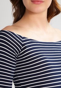 Marineblau und weiß gestreiftes Off-Shoulder-Oberteil, hergestellt aus einem Baumwollmischgewebe mit glatter Textur und taillierter Silhouette.