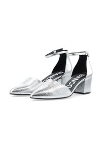 Chaussures à talons hauts argentées avec un bout pointu, un dessus texturé, une lanière de cheville et un talon bloc. L'intérieur a une semelle noire avec une marque.