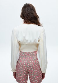 Weißes Langarmoberteil mit gepufften Ärmeln und gerafftem Rücken, kombiniert mit rosa Shorts mit einem kräftigen Leopardenmuster.