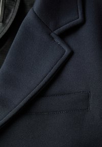Navy Blazer-Detail mit strukturiertem Stoff, scharfem Revers und kleiner Tasche mit sauberen Nähten und strukturiertem Design.