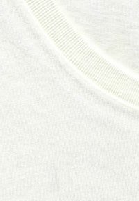 Light cream-colored textured fabric with a smooth surface. Features a ribbed round neckline and subtle variations in color.