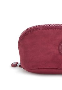 Borsa di stoffa bordeaux a forma arrotondata, con chiusura a zip e dettaglio del logo circolare. Texture liscia e cuciture della zip in contrasto.