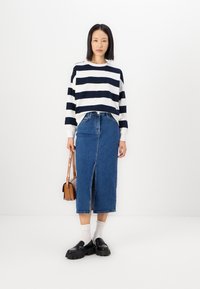 Randig marinblå och vit tröja i kombination med en blå jeanskjol med en framklippning. Svarta klumpiga skor och en liten brun crossbody-väska.