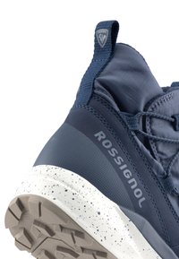 Modrá sportovní bota s texturovaným svrchním materiálem, zesílenou patou a bílou skvrnitou mezipodešví s vyvýšeným gumovým vzorkem.