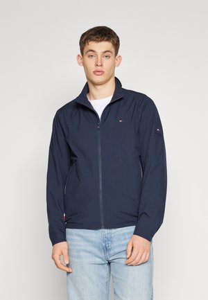 Giacca zip-up blu navy con collare alto, tessuto misto, tasche laterali e logo discreto sul petto e sul maniche. Vestibilità casual.