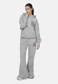 Graue Kapuzenjacke und ausgeflockte Jogginghose, aus weichem Stoff, mit einem dunkelgrauen Logo-Print auf der Brust und der Seite.