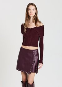 Burgunderfarbenes, gestricktes, schulterfreies Crop-Top, kombiniert mit einem hoch taillierten Lederrock mit silbernen Beschlägen und diagonaler Druckknopffunktion.