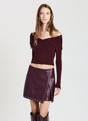 Top corto a maglia bordeaux con spalle scoperte abbinato a una gonna in pelle alta in vita con minuteria argentata e dettaglio a pressione diagonale.