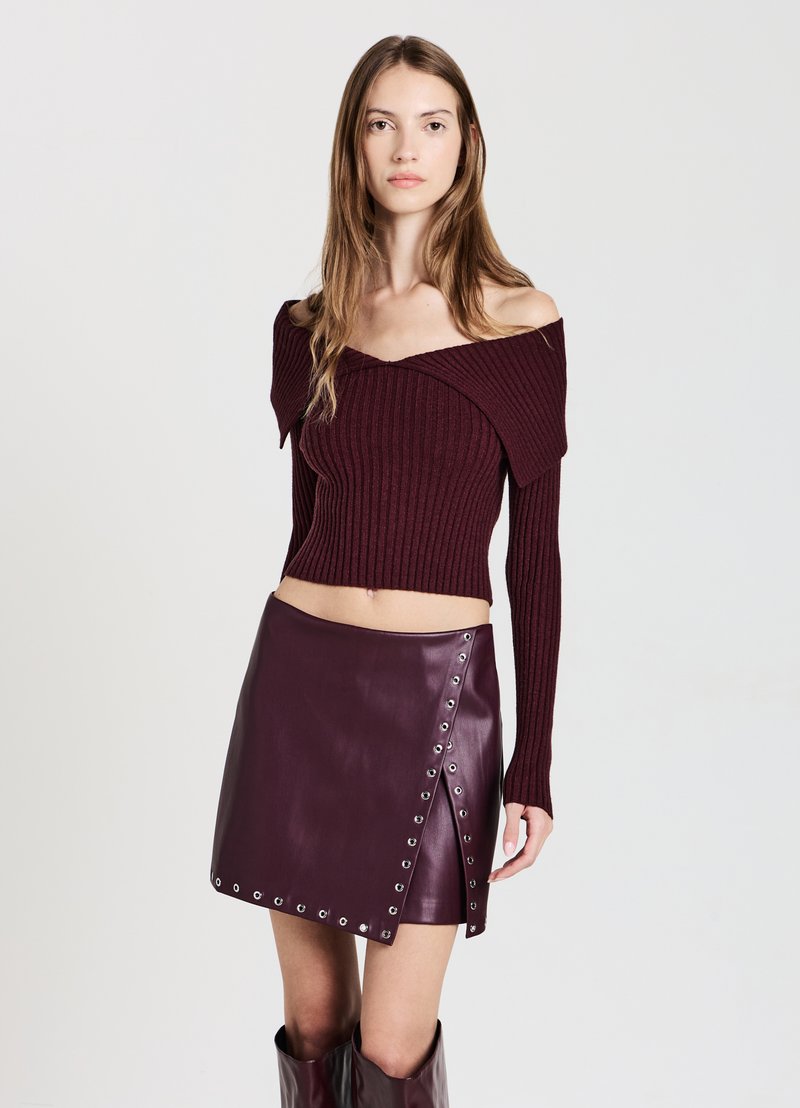 Burgunderfarbenes, gestricktes, schulterfreies Crop-Top, kombiniert mit einem hoch taillierten Lederrock mit silbernen Beschlägen und diagonaler Druckknopffunktion.