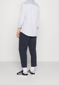 Ljusblå långärmad skjorta med en mörkblå axelpanel, matchad med marinblå byxor och svarta sneakers med vita ränder.