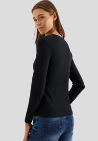 Svart långärmad topp med rund halsringning. Slät bomullsmix, åtsittande design, minimala sömmar och baksidan synlig. Tillsammans med blå jeans.