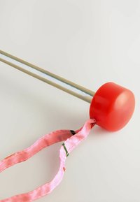 Rød plastikhåndtag med en cirkulær form fastgjort til en sølvmetalstang; har et pink bånd med grønne og røde accenter.