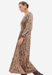 Dlouhé, splývavé šaty z měkké tkaniny s květinovým potiskem v tlumených barvách. Mají dlouhé rukávy, přiléhavý korzet a nařasený pas.