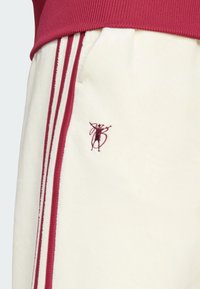 Kremfargede fleecebukser med maroon striper og et brodert logo. Livvidden er ribbet, noe som forbedrer tekstur og passform.