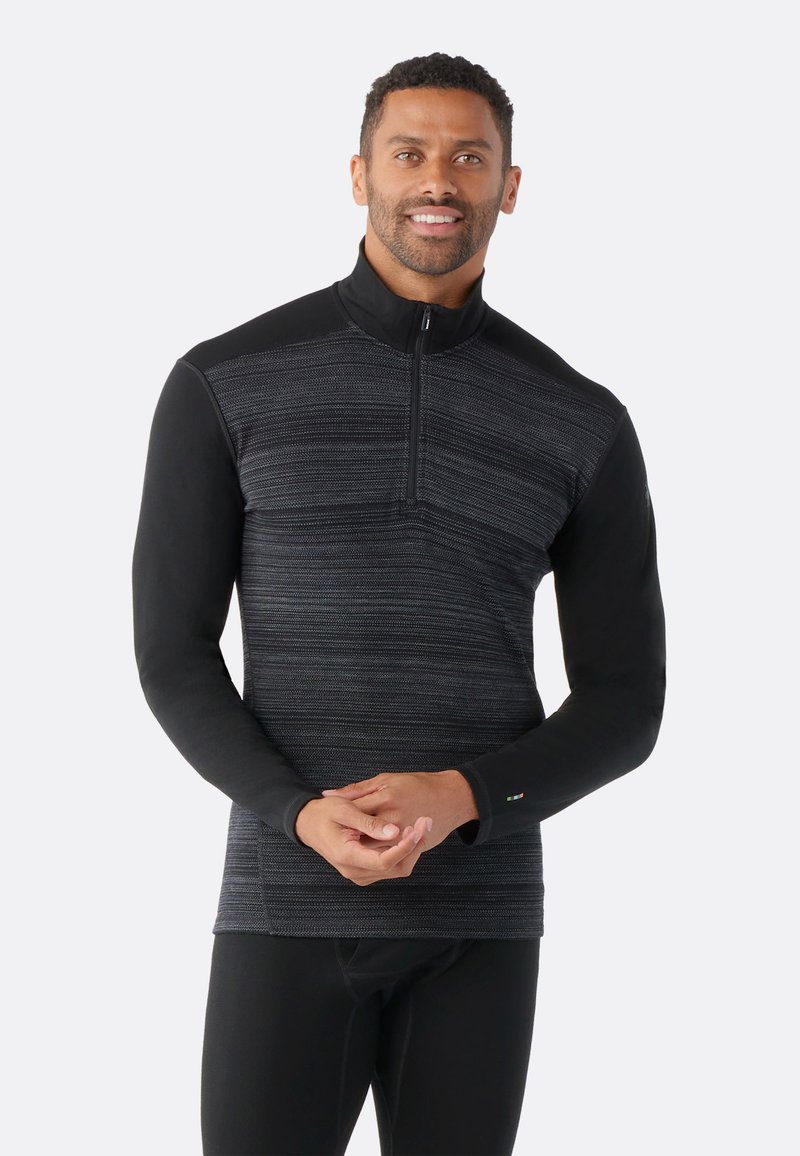Haut zippé noir à manches longues pour homme, arbore un motif texturé gris, des panneaux d'épaules noirs lisses et des accents de logo discrets sur le poignet.