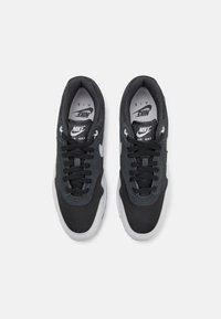 Baskets en mesh noir avec accents gris, bout rond et semelle blanche. Présente des lacets noirs et une marque sur la languette et sur le côté.