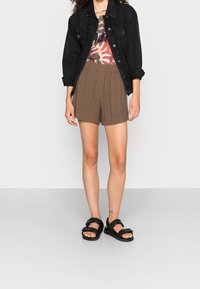 Svart denimjacka, mönstrad t-shirt i varma toner, bruna högmidjade shorts och svarta sandaler med spänne.