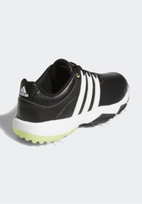 Czarne buty golfowe ze gładką skórzaną cholewką, trzema białymi paskami, zielonym akcentem na podeszwie oraz teksturowanym obcasem dla lepszej przyczepności.