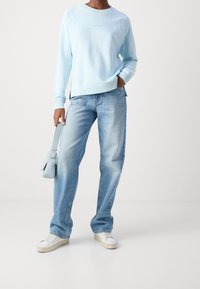 Sudadera de color azul claro con un corte relajado, combinada con jeans rectos de lavado claro y zapatillas blancas. El conjunto incluye un bolso pequeño azul.