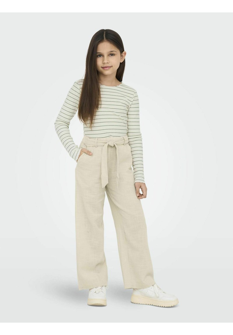 Randig långärmad skjorta i ljuskräm med gröna linjer; lösa beige byxor med midjebälte; vita sneakers; enkelt design.