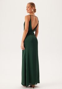 Zelené saténové maxi šaty s nízkým výstřihem na zádech, tenkými ramínky a přiléhavým korzetem. Hladká textura s volným střihem.