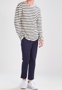 T-shirt z długim rękawem w kolorze kremowym i czarnym w paski, połączony z granatowymi spodniami o tapered fit i białymi sneakersami. Luźny krój, materiał mieszanki bawełny.