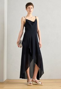 Black midi dress with cowl neck, thin straps, and metallic accents. Sheer lower hem; worn with gold espadrille sandals and a silver clutch.