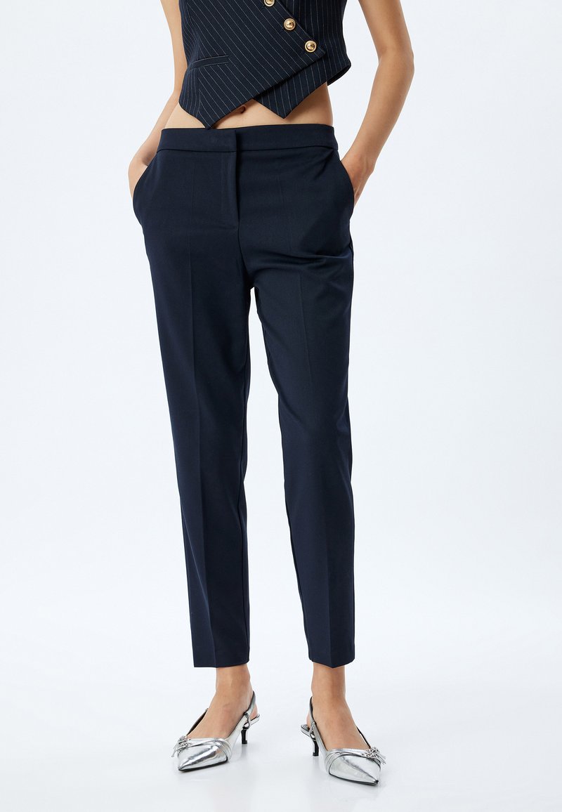 Marineblaue, taillierte Hose mit schmalem Schnitt, seitlichen Taschen und einem glatten, strukturierten Stoff. Kombiniert mit silbernen Absatzschuhen.