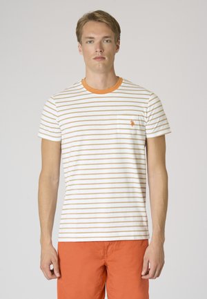 Uomo con indosso una maglietta a righe bianche e beige con colletto arancione e pantaloncini arancioni, in piedi davanti a uno sfondo chiaro e uniforme.