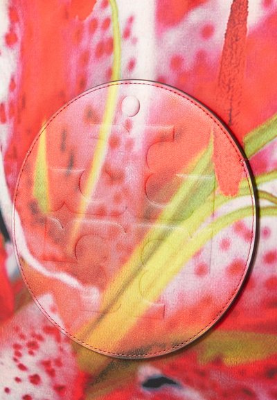 Okrągły, przejrzysty materiał z wytłaczanym wzorem puzzli w delikatnych odcieniach różu i pomarańczy, nałożony na intensywnie kwiecisty tle.